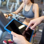 close up of trainer hands with tablet pc in gym