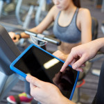 close up of trainer hands with tablet pc in gym