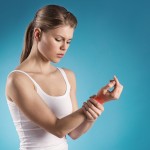 Young woman holding her painful wrist over blue background